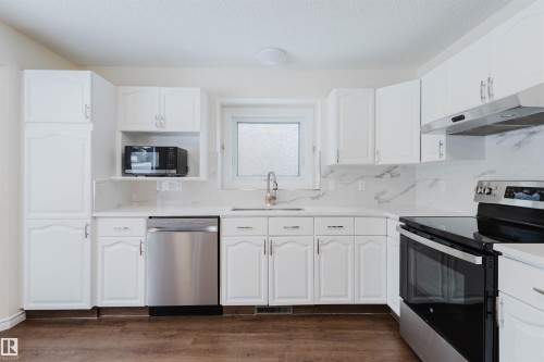Kitchen featuring stainless steel appliances, white cabinetry, backsplash, light stone counters, and a textured ceiling - 243 Rhatigan Road E, Edmonton, AB - Indoor Photo Showing Kitchen With Stainless Steel Kitchen