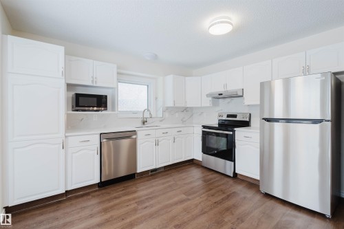 Kitchen featuring stainless steel appliances, white cabinets, dark wood finished floors, backsplash, and a textured ceiling - 243 Rhatigan Road E, Edmonton, AB - Indoor Photo Showing Kitchen With Stainless Steel Kitchen