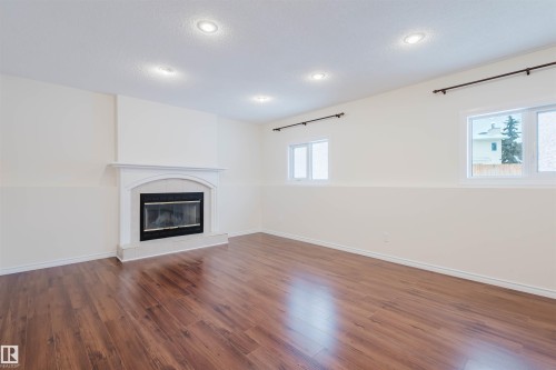 Unfurnished living room featuring a fireplace, dark wood-type flooring, healthy amount of natural light, and recessed lighting - 243 Rhatigan Road E, Edmonton, AB - Indoor Photo Showing Living Room With Fireplace