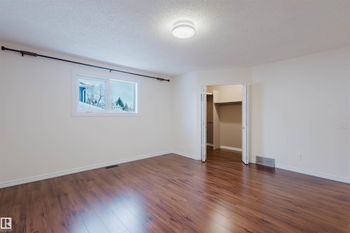 Unfurnished bedroom featuring a walk in closet, a textured ceiling, and dark wood finished floors - 243 Rhatigan Road E, Edmonton, AB - Indoor Photo Showing Other Room