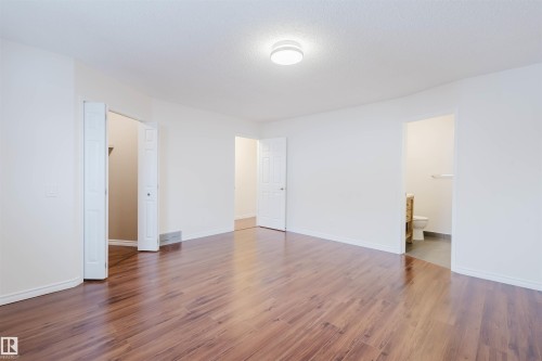 Unfurnished bedroom with dark wood-type flooring, ensuite bathroom, and a textured ceiling - 243 Rhatigan Road E, Edmonton, AB - Indoor Photo Showing Other Room