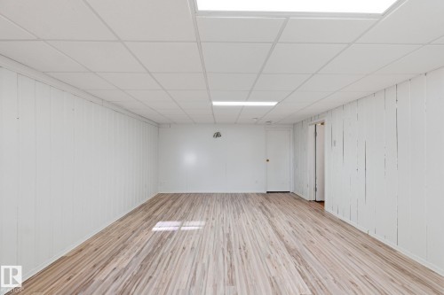 Unfurnished room with a paneled ceiling, light wood-style flooring, and wooden walls - 12225 134 Street, Edmonton, AB - Indoor Photo Showing Other Room
