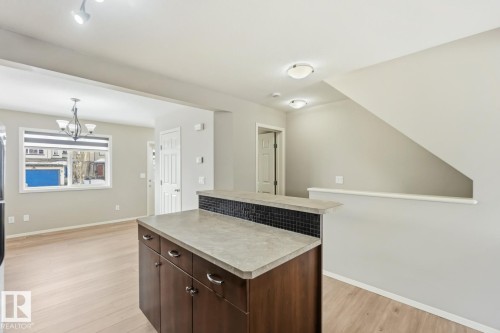 Kitchen with dark wood finish cabinetry, a kitchen island, light countertops, light wood finished floors, and suspended lighting - 16 3751 12 Street, Edmonton, AB - Indoor Photo Showing Other Room