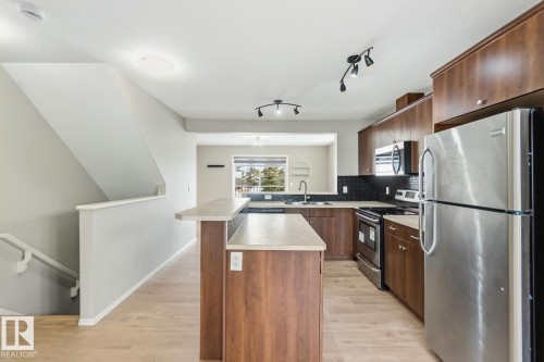Kitchen with stainless steel appliances, light countertops, light wood-style flooring, tasteful backsplash, and track lighting - 16 3751 12 Street, Edmonton, AB - Indoor Photo Showing Kitchen With Stainless Steel Kitchen