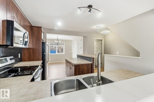Kitchen featuring stainless steel appliances, light countertops, light wood-type flooring, a chandelier, and a center island - 16 3751 12 Street, Edmonton, AB - Indoor Photo Showing Kitchen With Double Sink