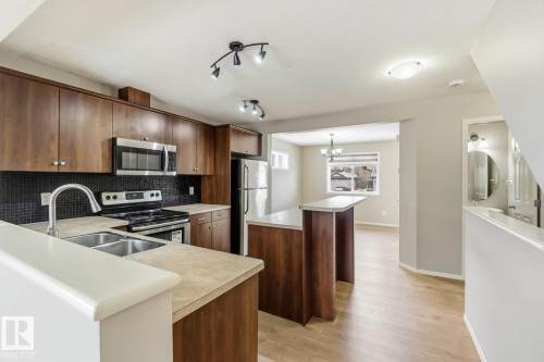 Kitchen with a center island, stainless steel appliances, light wood finished floors, light countertops, and backsplash - 16 3751 12 Street, Edmonton, AB - Indoor Photo Showing Kitchen With Stainless Steel Kitchen With Double Sink