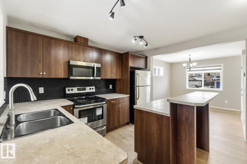 Kitchen featuring stainless steel appliances, dark wood finish cabinetry, light countertops, a center island, and decorative backsplash - 16 3751 12 Street, Edmonton, AB - Indoor Photo Showing Kitchen With Stainless Steel Kitchen With Double Sink With Upgraded Kitchen