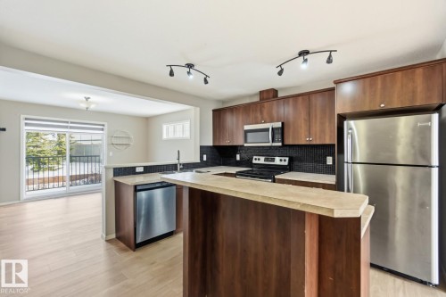 Kitchen with stainless steel appliances, light countertops, a kitchen island, light wood-style floors, and tasteful backsplash - 16 3751 12 Street, Edmonton, AB - Indoor Photo Showing Kitchen With Stainless Steel Kitchen