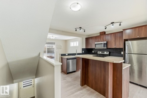 Kitchen featuring stainless steel appliances, a kitchen island, light countertops, tasteful backsplash, and light wood-style flooring - 16 3751 12 Street, Edmonton, AB - Indoor Photo Showing Kitchen With Stainless Steel Kitchen