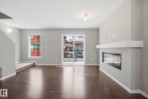 Unfurnished living room with a glass covered fireplace, dark wood-style flooring, and a textured ceiling - 71 4029 Orchards Drive, Edmonton, AB - Indoor Photo Showing Living Room With Fireplace