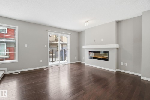 Unfurnished living room featuring dark wood finished floors and a glass covered fireplace - 71 4029 Orchards Drive, Edmonton, AB - Indoor Photo Showing Living Room With Fireplace