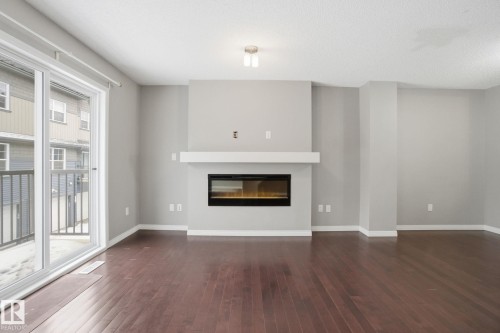 Unfurnished living room featuring a glass covered fireplace and dark wood finished floors - 71 4029 Orchards Drive, Edmonton, AB - Indoor Photo Showing Living Room With Fireplace