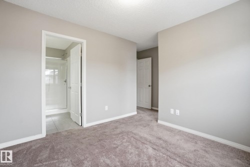 Unfurnished bedroom featuring light colored carpet, a textured ceiling, and ensuite bathroom - 71 4029 Orchards Drive, Edmonton, AB - Indoor Photo Showing Other Room