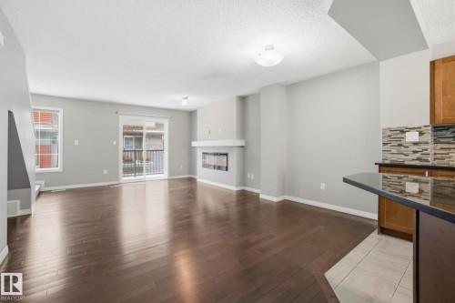 Unfurnished living room featuring dark wood-style floors, a textured ceiling, and a glass covered fireplace - 71 4029 Orchards Drive, Edmonton, AB - Indoor Photo Showing Living Room