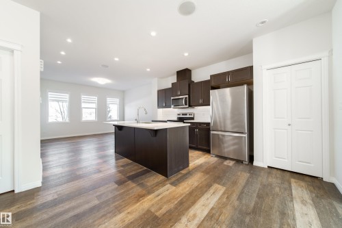 Kitchen featuring stainless steel appliances, dark wood finish cabinetry, a kitchen breakfast bar, decorative backsplash, and a center island with sink - 1199 Watt Drive, Edmonton, AB - Indoor Photo Showing Kitchen With Upgraded Kitchen