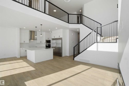 Kitchen featuring white cabinetry, stainless steel appliances, light wood-style flooring, a kitchen island with sink, and a high ceiling - 6949 176A Avenue, Edmonton, AB - Indoor Photo Showing Kitchen