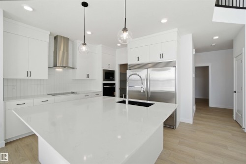 Kitchen with backsplash, stainless steel built in refrigerator, light wood-type flooring, white cabinets, and decorative light fixtures - 6949 176A Avenue, Edmonton, AB - Indoor Photo Showing Kitchen With Upgraded Kitchen