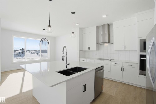 Kitchen featuring light wood-type flooring, white cabinets, an island with sink, and hanging light fixtures - 6949 176A Avenue, Edmonton, AB - Indoor Photo Showing Kitchen With Double Sink With Upgraded Kitchen