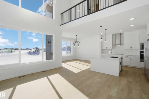 Kitchen with white cabinetry, modern cabinets, light wood-style flooring, a kitchen island with sink, and a high ceiling - 6949 176A Avenue, Edmonton, AB - Indoor Photo Showing Kitchen With Upgraded Kitchen