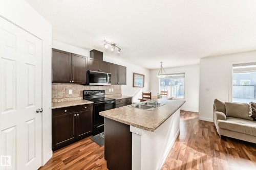 Kitchen featuring black range with electric stovetop, dark wood finish cabinetry, a center island with sink, backsplash, and light countertops - 17357 8A Avenue, Edmonton, AB 