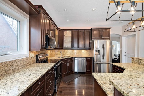 Kitchen featuring dark wood finish cabinets, stainless steel appliances, glass insert cabinets, dark wood finished floors, and arched walkways - 10623 75 Avenue, Edmonton, AB - Indoor Photo Showing Kitchen With Double Sink With Upgraded Kitchen