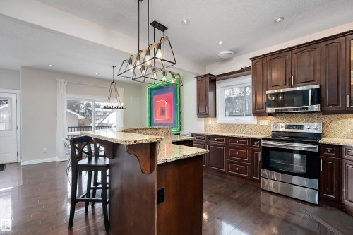 Kitchen with stainless steel appliances, backsplash, dark wood finish cabinetry, and light stone countertops - 10623 75 Avenue, Edmonton, AB - Indoor Photo Showing Kitchen With Upgraded Kitchen