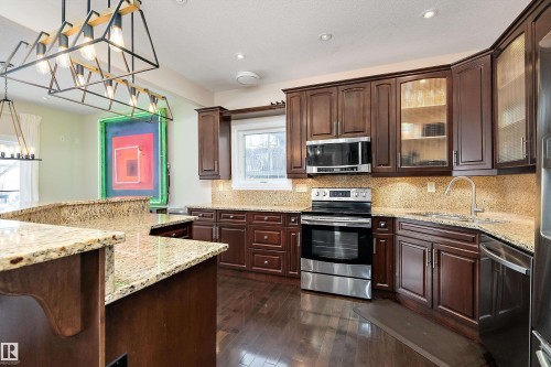 Kitchen with pendant lighting, stainless steel appliances, backsplash, dark wood finish cabinetry, and light stone countertops - 10623 75 Avenue, Edmonton, AB - Indoor Photo Showing Kitchen With Upgraded Kitchen