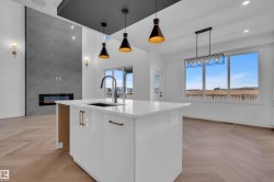 Kitchen featuring parquet flooring, an island with sink, decorative light fixtures, a large fireplace, and light stone countertops - 