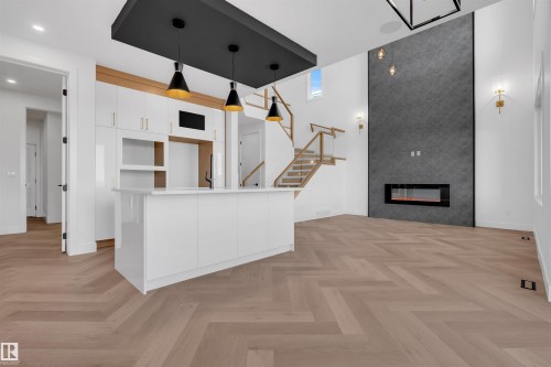 Kitchen featuring white cabinetry, parquet floors, a spacious island, hanging light fixtures, and a large fireplace - 108 Eldridge Point(E), St. Albert, AB - Indoor With Fireplace
