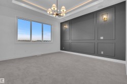 Empty room with a decorative wall, a tray ceiling, light carpet, and suspended lighting - 