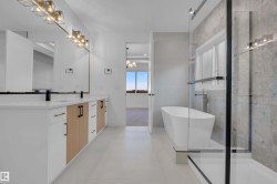 Bathroom featuring double vanity, a soaking tub, a shower stall, and suspended lighting - 