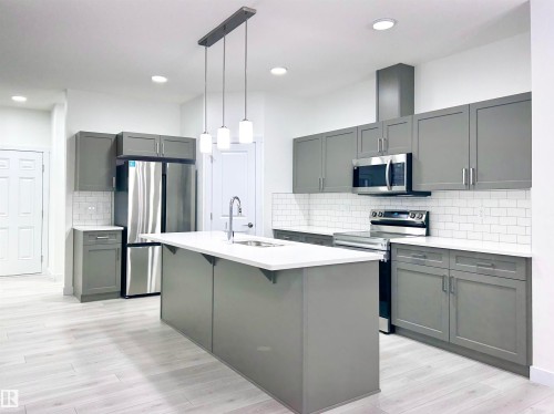 Kitchen with stainless steel appliances, gray cabinetry, a center island with sink, light wood-style floors, and a kitchen bar - 19704 29 Avenue, Edmonton, AB - Indoor Photo Showing Kitchen With Upgraded Kitchen