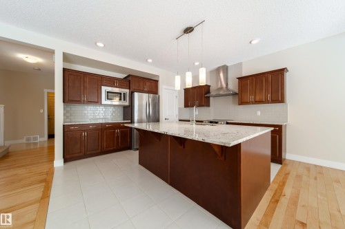 Kitchen with backsplash, light stone countertops, a breakfast bar, a kitchen island with sink, and a textured ceiling - 2237 56 Street, Edmonton, AB - Indoor Photo Showing Kitchen With Double Sink