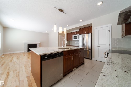 Kitchen with stainless steel appliances, a center island with sink, light stone counters, extractor fan, and hanging light fixtures - 2237 56 Street, Edmonton, AB - Indoor Photo Showing Kitchen With Stainless Steel Kitchen