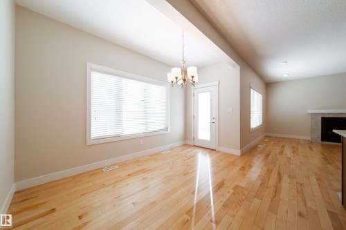 Unfurnished dining area with hanging lights, light wood-style floors, a tile fireplace, and a textured ceiling - 2237 56 Street, Edmonton, AB - Indoor Photo Showing Other Room