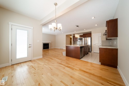 Kitchen with open floor plan, a center island with sink, a fireplace, light wood-style floors, and dark wood finish cabinets - 2237 56 Street, Edmonton, AB - Indoor Photo Showing Kitchen