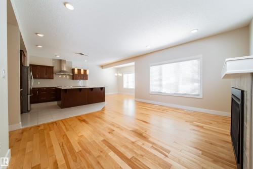 Unfurnished living room with light wood finished floors, a fireplace, and suspended lighting - 2237 56 Street, Edmonton, AB - Indoor