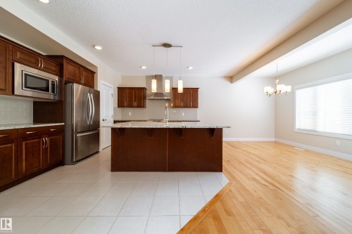 Kitchen featuring a breakfast bar, stainless steel appliances, hanging lights, light stone countertops, and a center island with sink - 2237 56 Street, Edmonton, AB - Indoor Photo Showing Kitchen