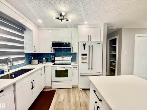 Kitchen with white appliances, light wood-style flooring, white cabinetry, recessed lighting, and backsplash - 2915 145 Avenue, Edmonton, AB - Indoor Photo Showing Kitchen With Double Sink