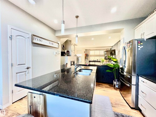 Kitchen with open floor plan, freestanding refrigerator, white cabinetry, dark stone countertops, and light wood-type flooring - 425 Sheppard Boulevard, Leduc, AB - Indoor Photo Showing Kitchen With Double Sink With Upgraded Kitchen