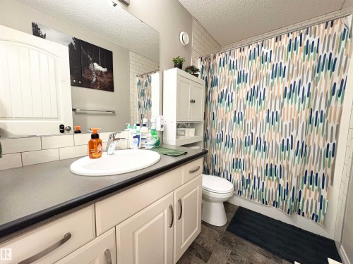 Bathroom with vanity, a textured ceiling, shower / bath combo with shower curtain, and dark stone finish flooring - 425 Sheppard Boulevard, Leduc, AB - Indoor Photo Showing Bathroom