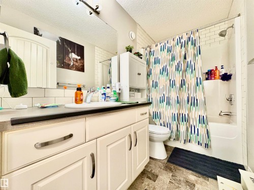 Bathroom with vanity, shower / bathtub combination with curtain, a textured ceiling, and stone finish floors - 425 Sheppard Boulevard, Leduc, AB - Indoor Photo Showing Bathroom