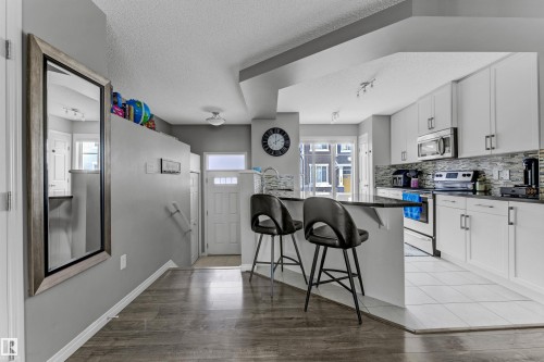 Kitchen featuring white cabinetry, a breakfast bar, stainless steel appliances, a textured ceiling, and a peninsula - #127 2905 141 Street, Edmonton, AB - Indoor Photo Showing Kitchen
