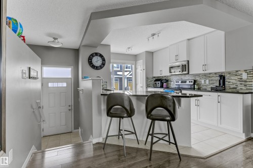 Kitchen featuring a textured ceiling, white cabinets, a breakfast bar area, tasteful backsplash, and light tile patterned floors - #127 2905 141 Street, Edmonton, AB - Indoor Photo Showing Kitchen With Upgraded Kitchen