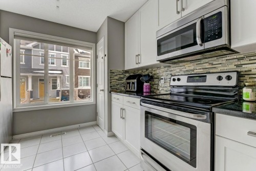 Kitchen featuring stainless steel appliances, white cabinets, light tile patterned floors, and a textured ceiling - #127 2905 141 Street, Edmonton, AB - Indoor Photo Showing Kitchen