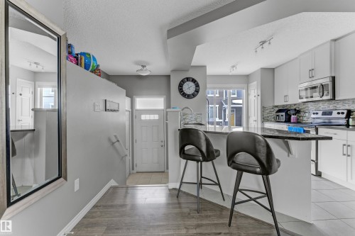 Kitchen with stainless steel appliances, white cabinetry, a kitchen bar, a textured ceiling, and decorative backsplash - #127 2905 141 Street, Edmonton, AB - Indoor Photo Showing Kitchen