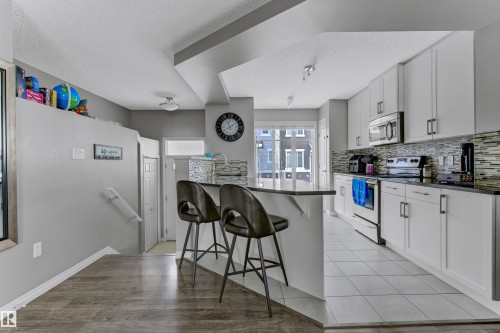 Kitchen featuring a breakfast bar area, stainless steel appliances, white cabinets, a textured ceiling, and a peninsula - #127 2905 141 Street, Edmonton, AB - Indoor Photo Showing Kitchen