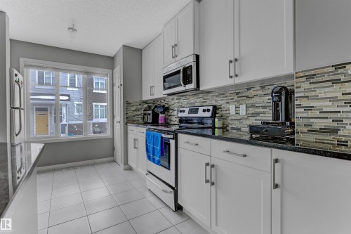 Kitchen featuring stainless steel appliances, white cabinets, dark stone countertops, light tile patterned flooring, and a textured ceiling - #127 2905 141 Street, Edmonton, AB - Indoor Photo Showing Kitchen With Upgraded Kitchen