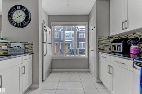 Kitchen featuring white cabinets, dark stone counters, freestanding refrigerator, backsplash, and light tile patterned floors - #127 2905 141 Street, Edmonton, AB - Indoor Photo Showing Kitchen
