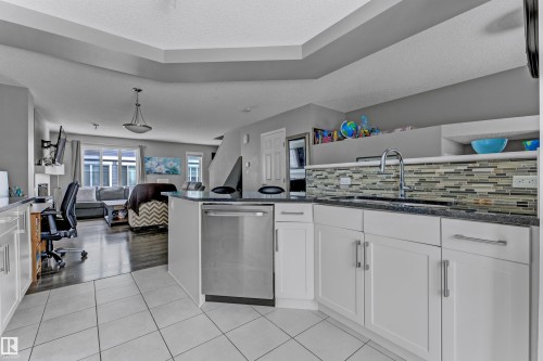 Kitchen with white cabinetry, dark stone counters, dishwasher, open floor plan, and light tile patterned flooring - #127 2905 141 Street, Edmonton, AB - Indoor Photo Showing Kitchen